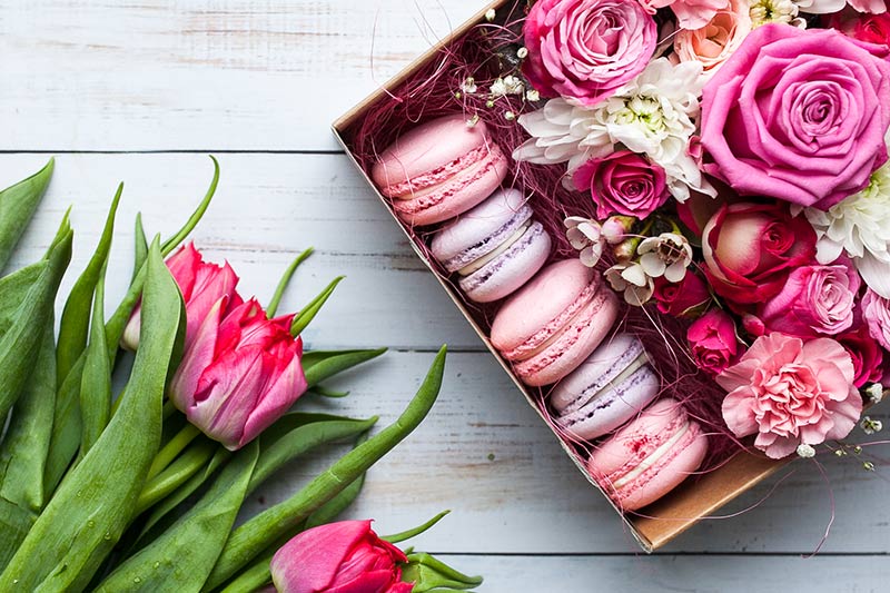 Box of pink and purple macaroons, daisies, carnations and pink roses with a bunch of red tulips