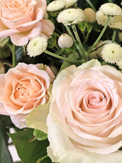 Focus on a pink rose in a pink and peach bouquet with white Veronica in a glass vase