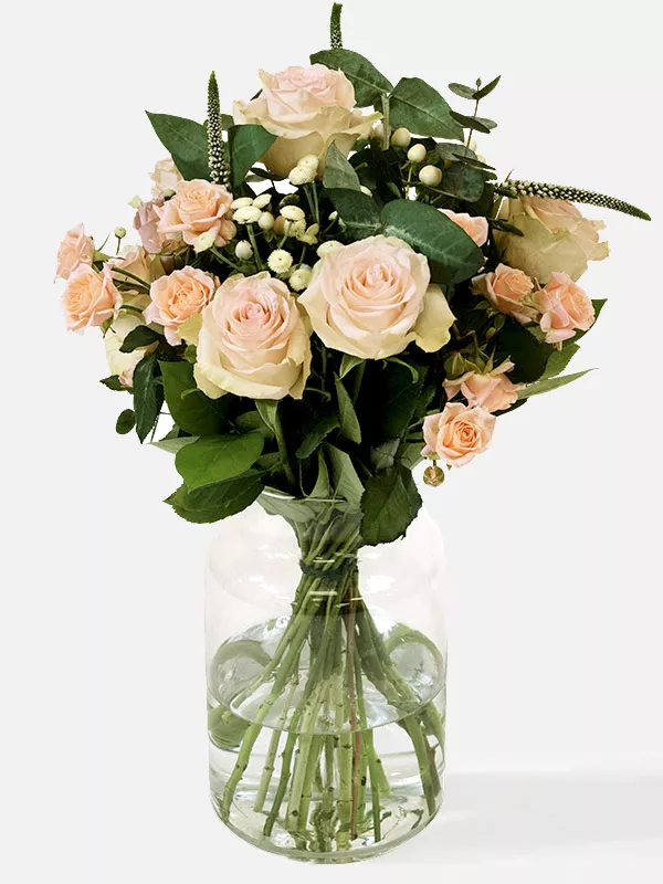 Focus on a pink rose in a pink and peach bouquet with white Veronica in a glass vase