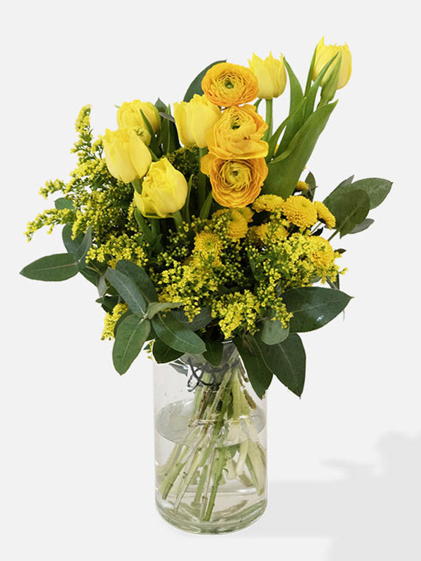 Mixed bunch of Yellow Tulips, Yellow Santini chrysanthemum, Yellow Ranunculus and Solidago in a glass vase